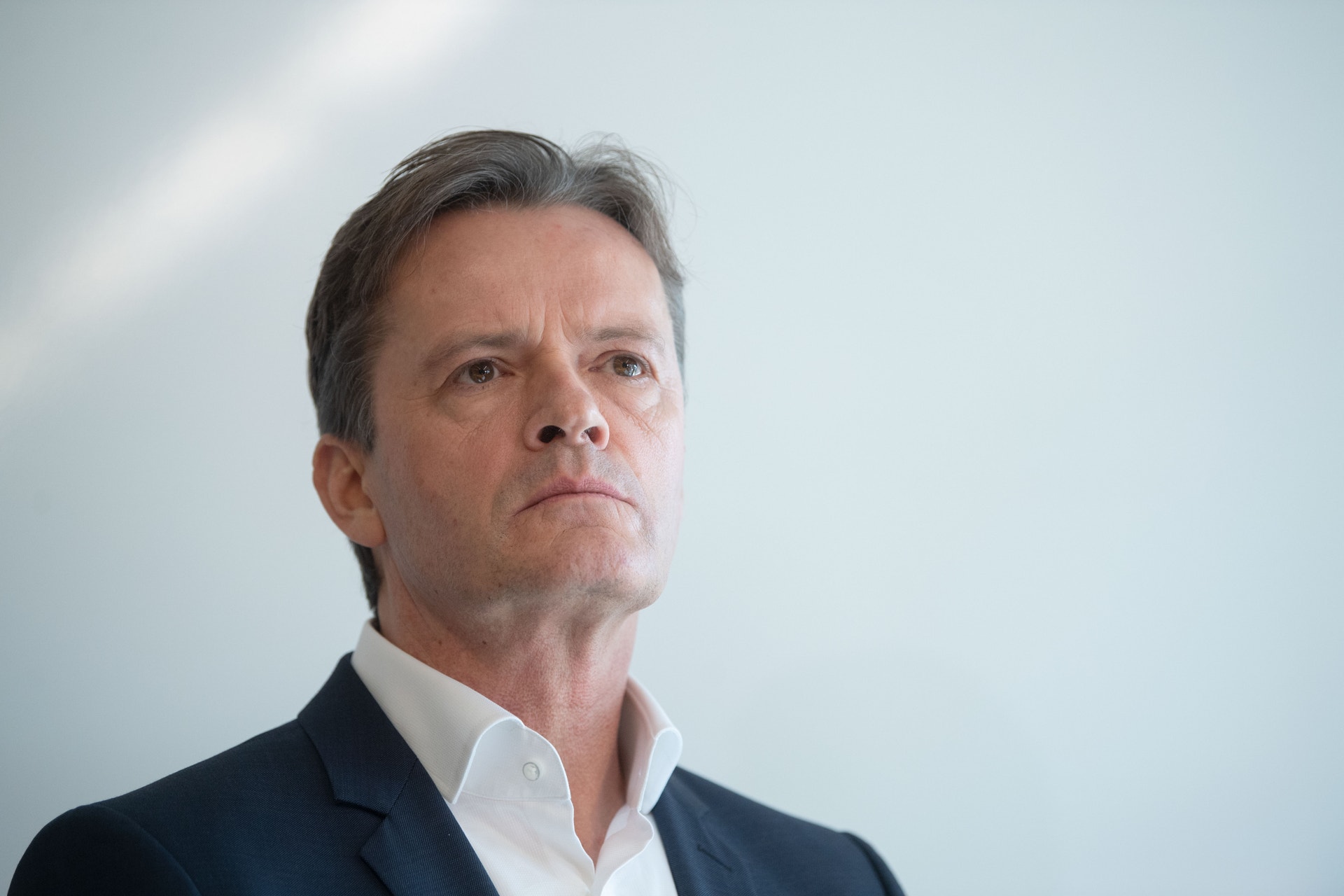 Porträtt av en man i mörkblå kavaj och vit skjorta mot ljus bakgrund.