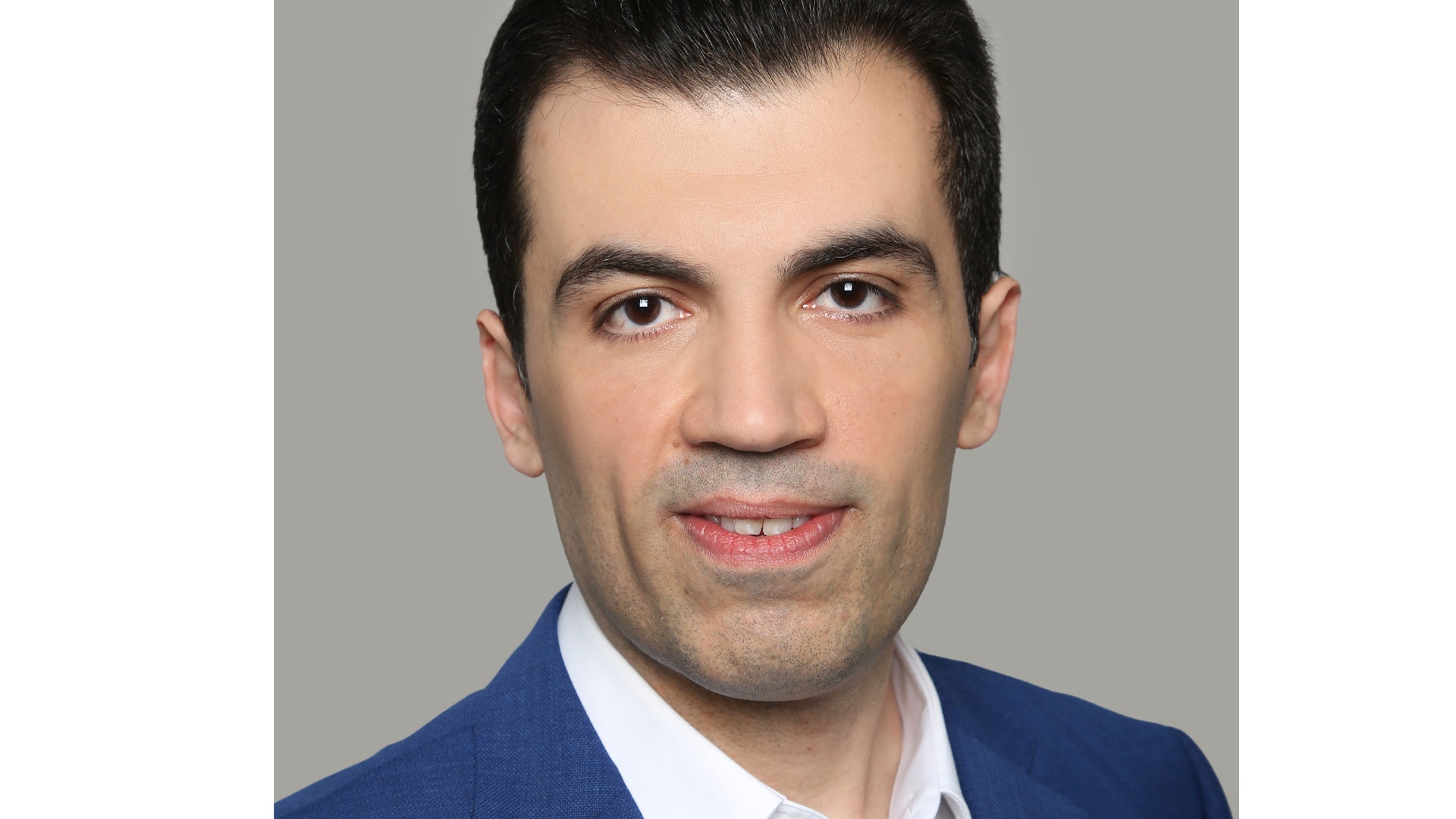 Porträttfoto av en man i mörkblå kavaj och vit skjorta mot grå bakgrund