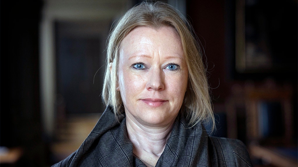 Porträtt av en kvinna med ljust hår, klädd i mörk jacka, fotograferad inomhus.