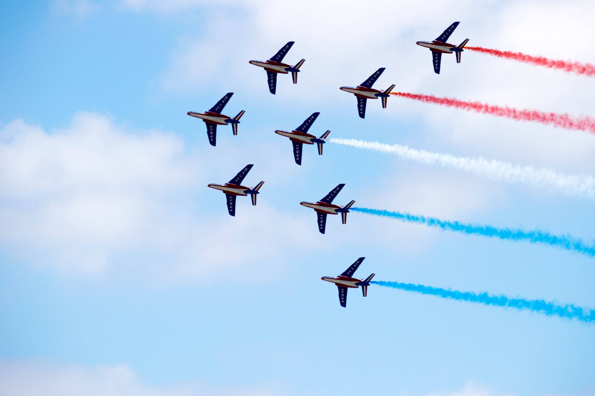 Åtta stridsflygplan flyger i formation mot blå himmel och lämnar efter sig röda, vita och blå rökspår.