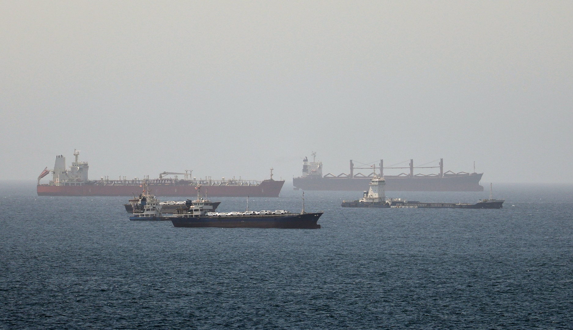 Tre stora lastfartyg på öppet hav vid Hormuz-sundet. Ett rött tankfartyg i bakgrunden, ett svart containerfartyg i förgrunden och ett större lastfartyg till höger.