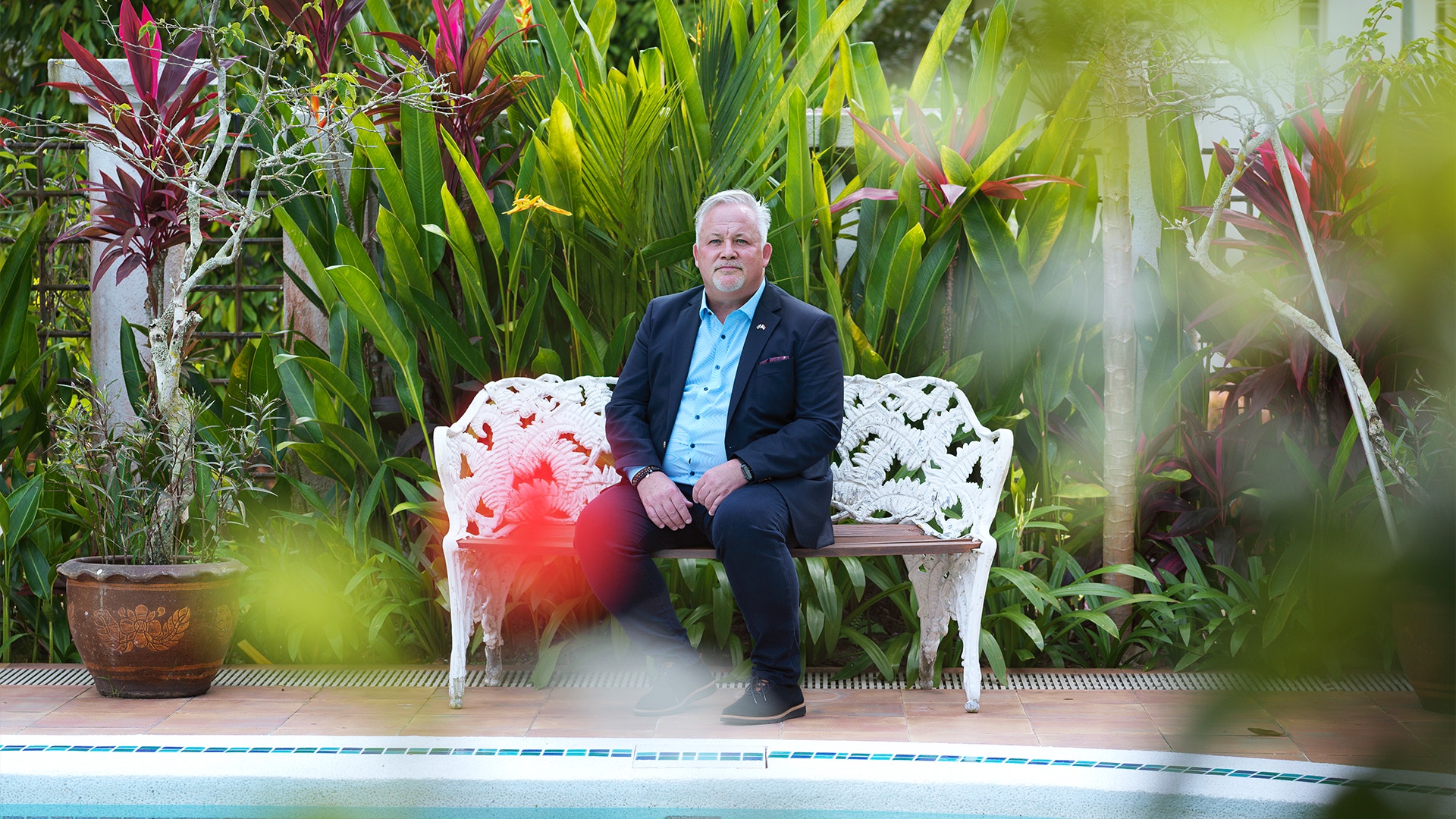 Kent Härstedt sitter på en bänk omgiven av grönskan i Singapore. Framför honom glittrar vattnet i polen. 