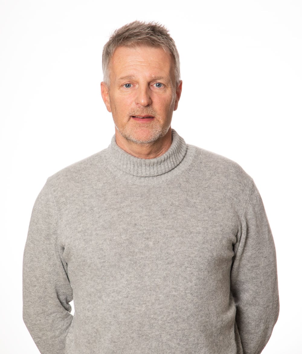 Porträtt av en man med kort ljust hår, iklädd en beige polotröja mot vit bakgrund.