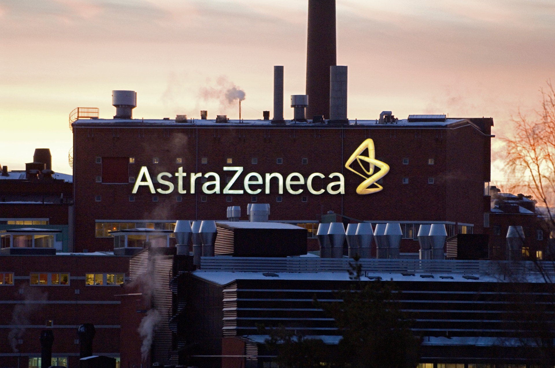 Industribyggnad med AstraZenecas logo och namn belyst på fasaden vid skymning.