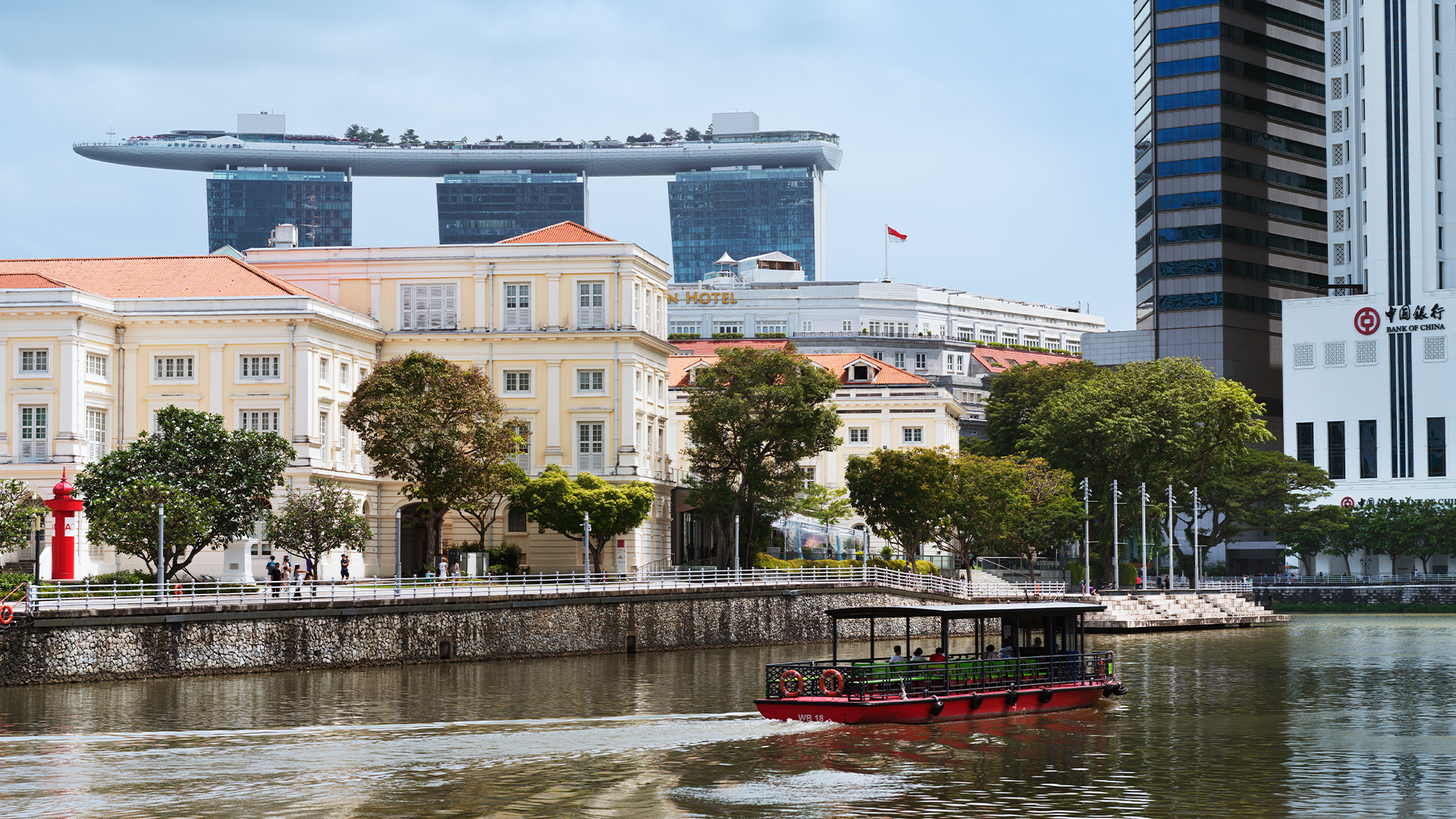 En båt glider genom en av kanalerna i Singapore. På andra sidan vattnet sträcker sig skyskrapor och europeiskt inspirerade fasader. 