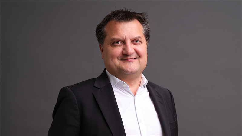 Porträtt av en man i mörk kostym och vit skjorta mot grå bakgrund