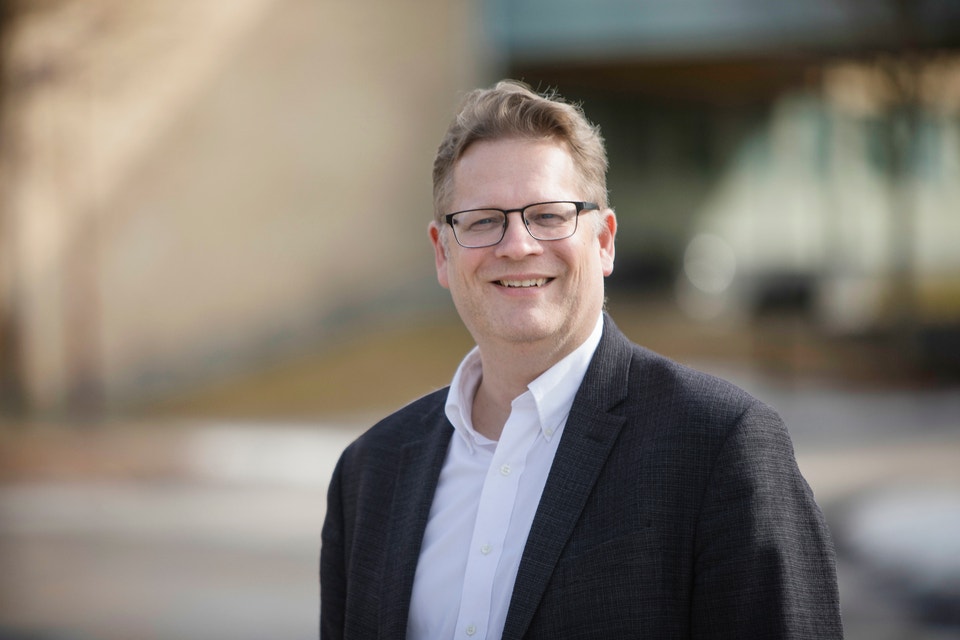 Porträtt av en man i mörk kavaj och vit skjorta som ler mot kameran.