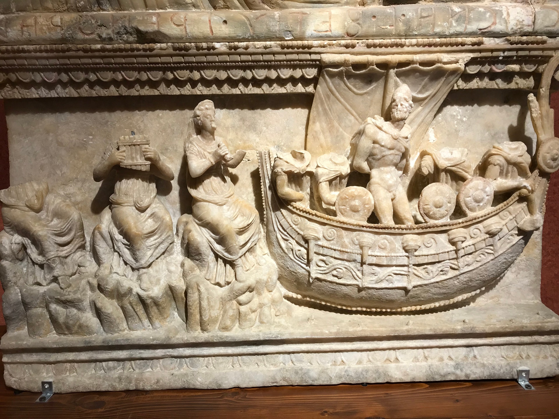 Antikt stenskulptur-relief som visar en scen från Odysseus-sagan. Till vänster står flera människofigurer, till höger syns ett antikt fartyg med människor ombord.