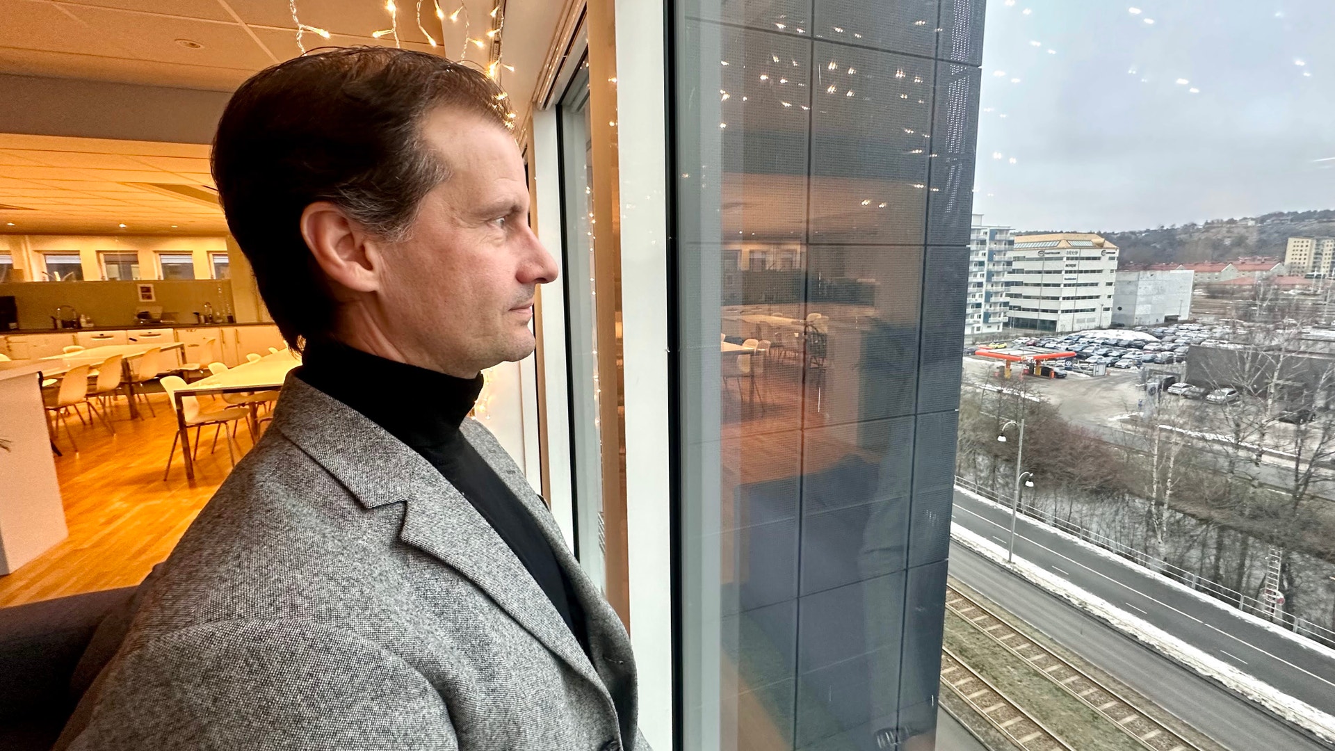 Klas Moreau tittar ut genom ett stort fönster från en höghus med stadsutsikt i bakgrunden