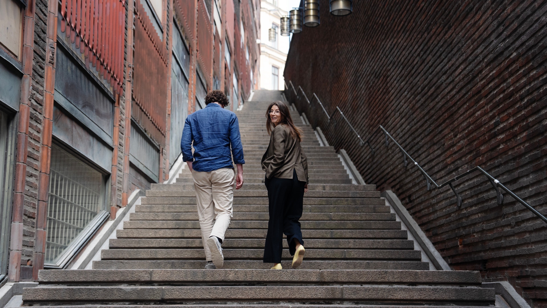 Hanna Andreen och Antonio Melani går upp för trapporna vid Kungsgatan, omringade av tegelfasader.