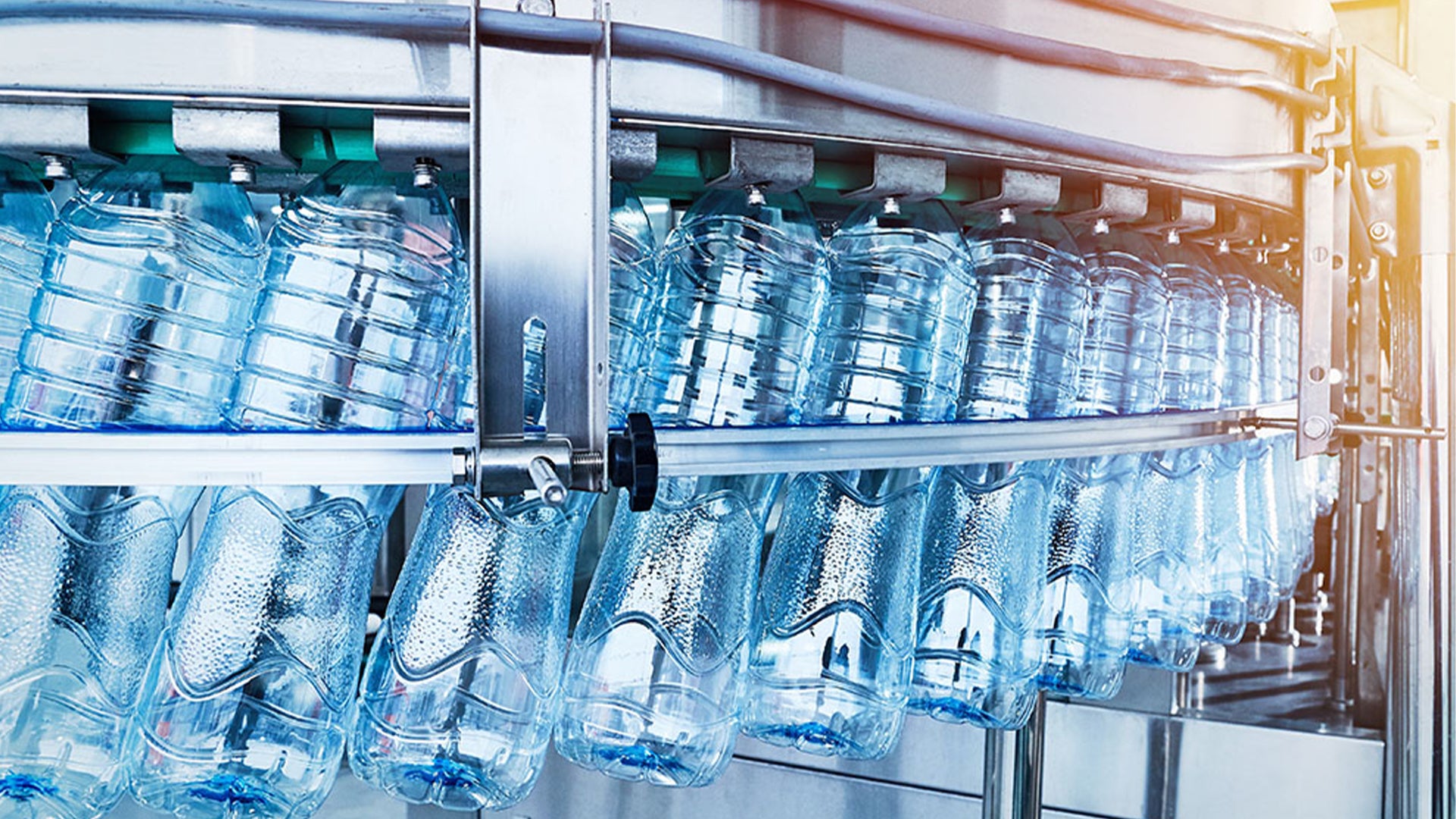 Flaskvatten på hyllor i en butik. Flera rader med plastflaskor innehållande vatten, både större och mindre flaskor.