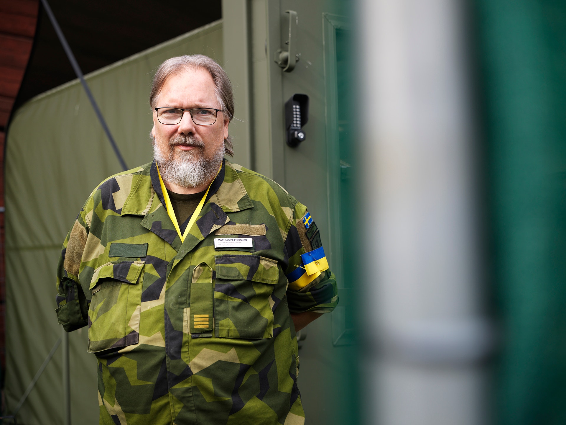 En man i militär kamouflageuniform står utanför ett tält.