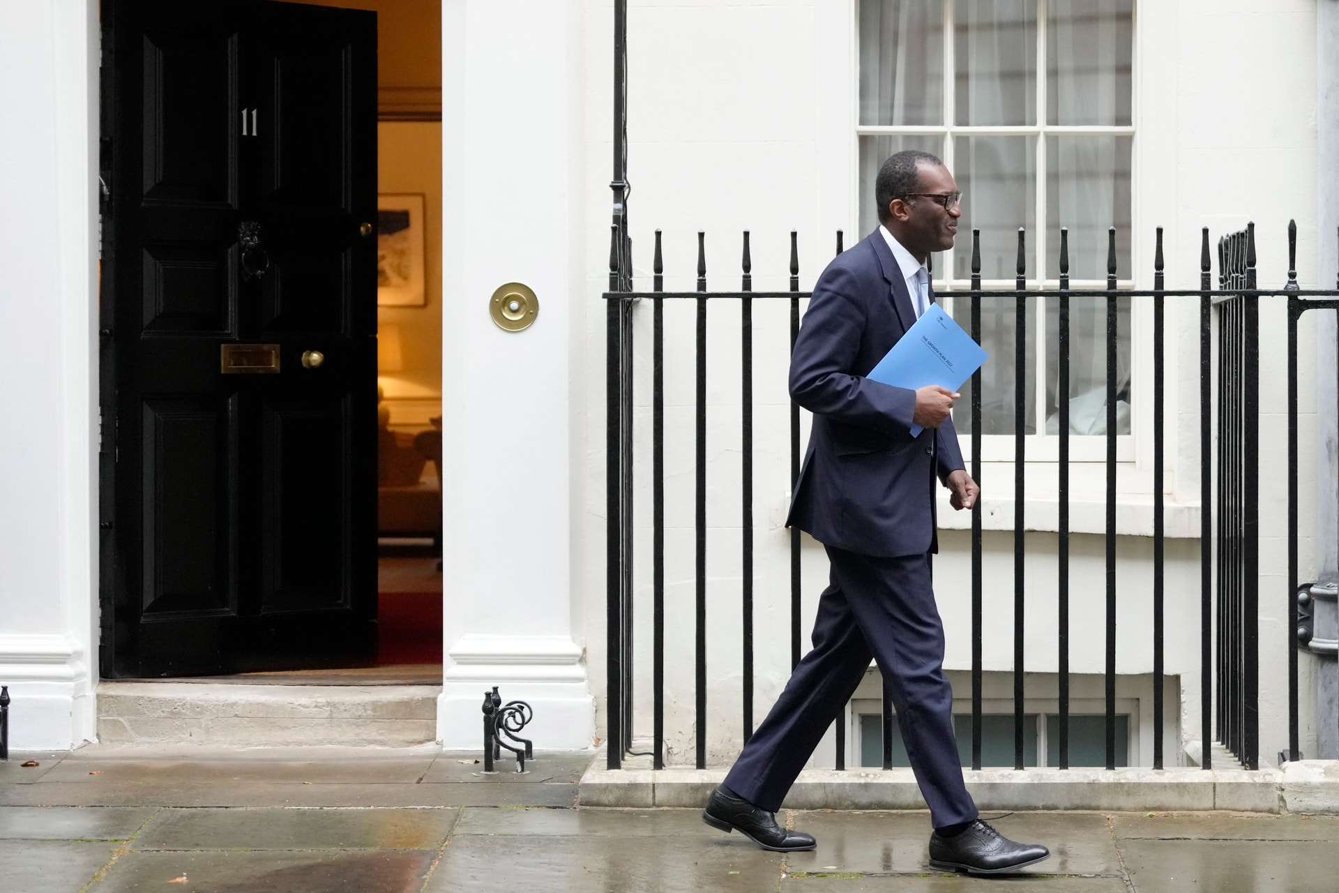 En man i kostym går ut genom en dörr på Downing Street 11 med en mapp under armen.