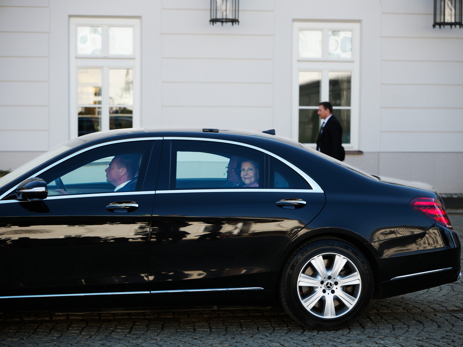 Svart lyxbil parkerad framför vit byggnad med passagerare i bilen