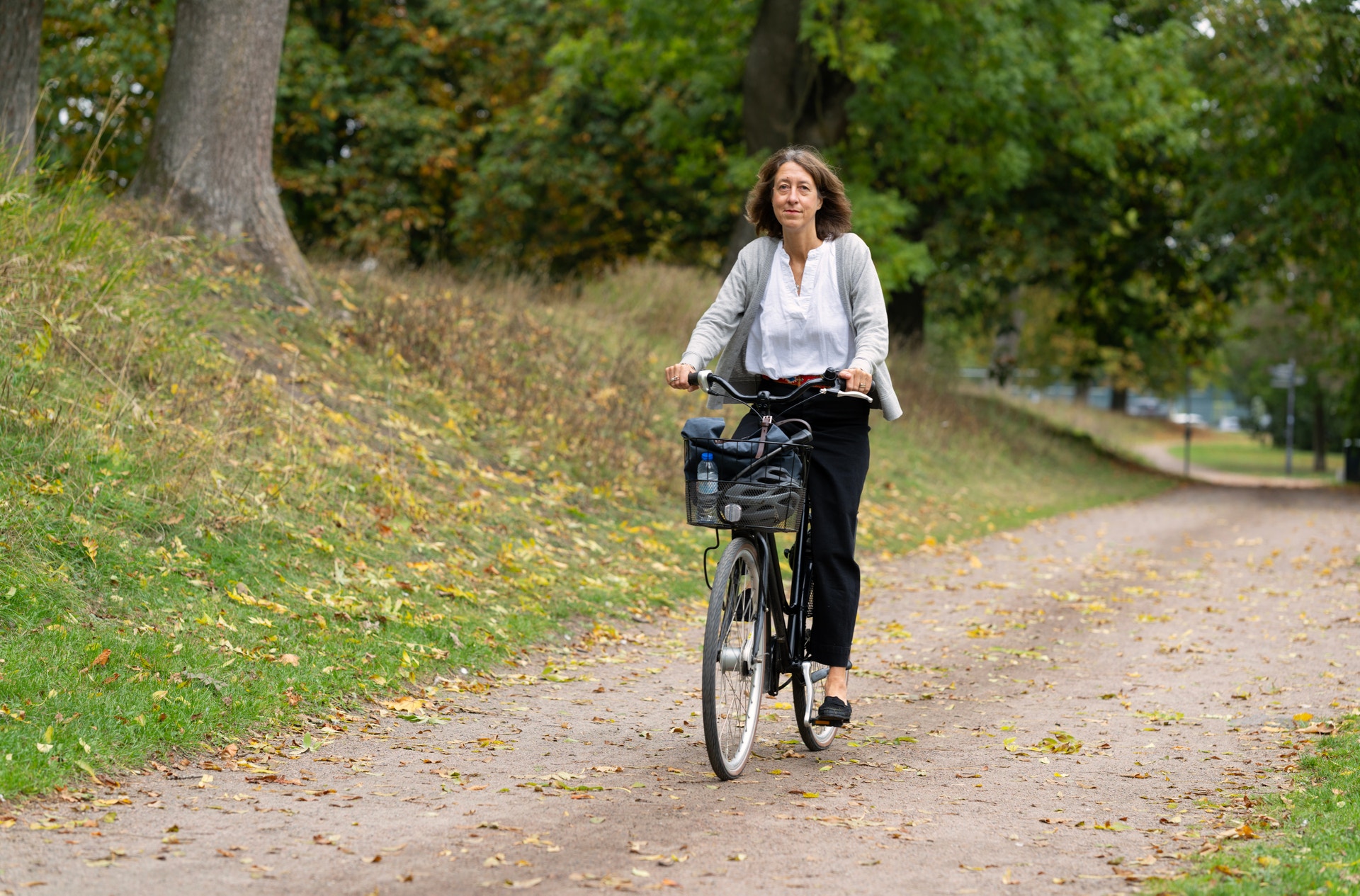 En kvinna cyklar på en grusväg genom en park på hösten.