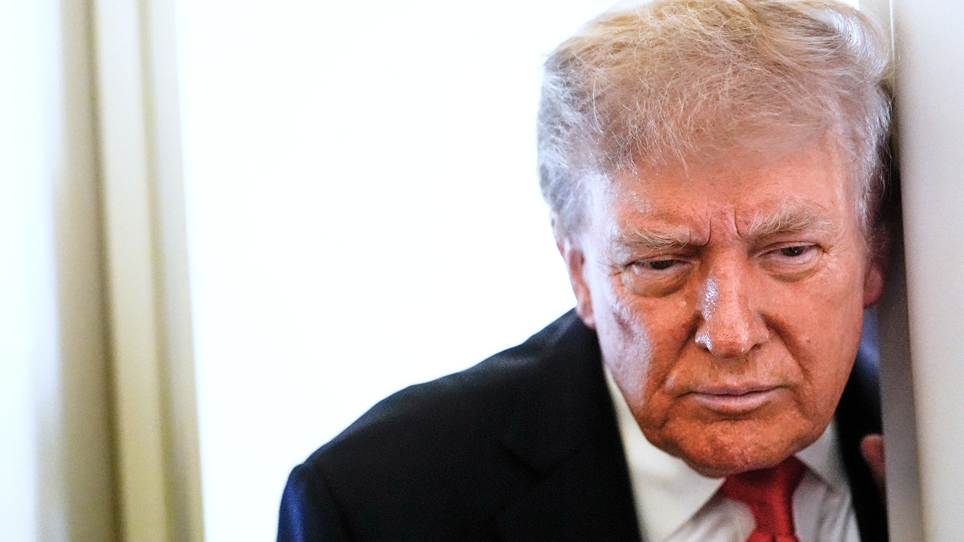 Donald Trump står och lutar sig mot en dörrkarm. Han tittar ner.