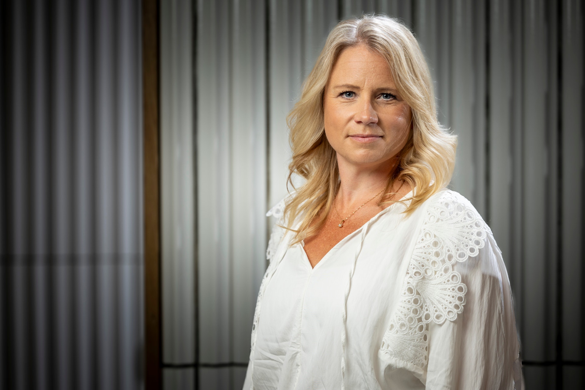 Porträtt av en kvinna med långt blont hår som bär en vit blus med spetsdetaljer.