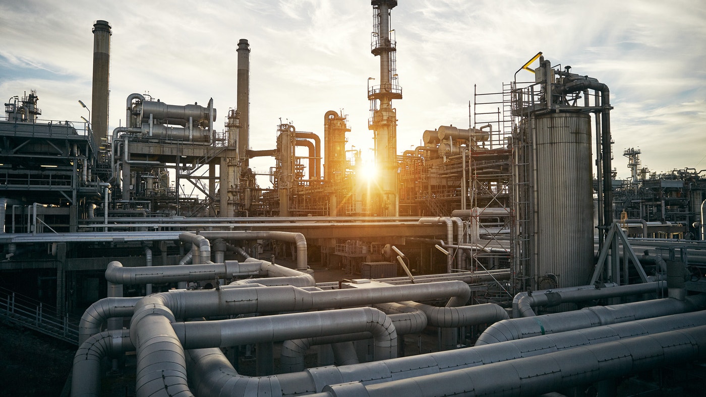 En stor raffineringsanläggning med industriella rör, torn och utrustning mot en molnig himmel vid solnedgång.